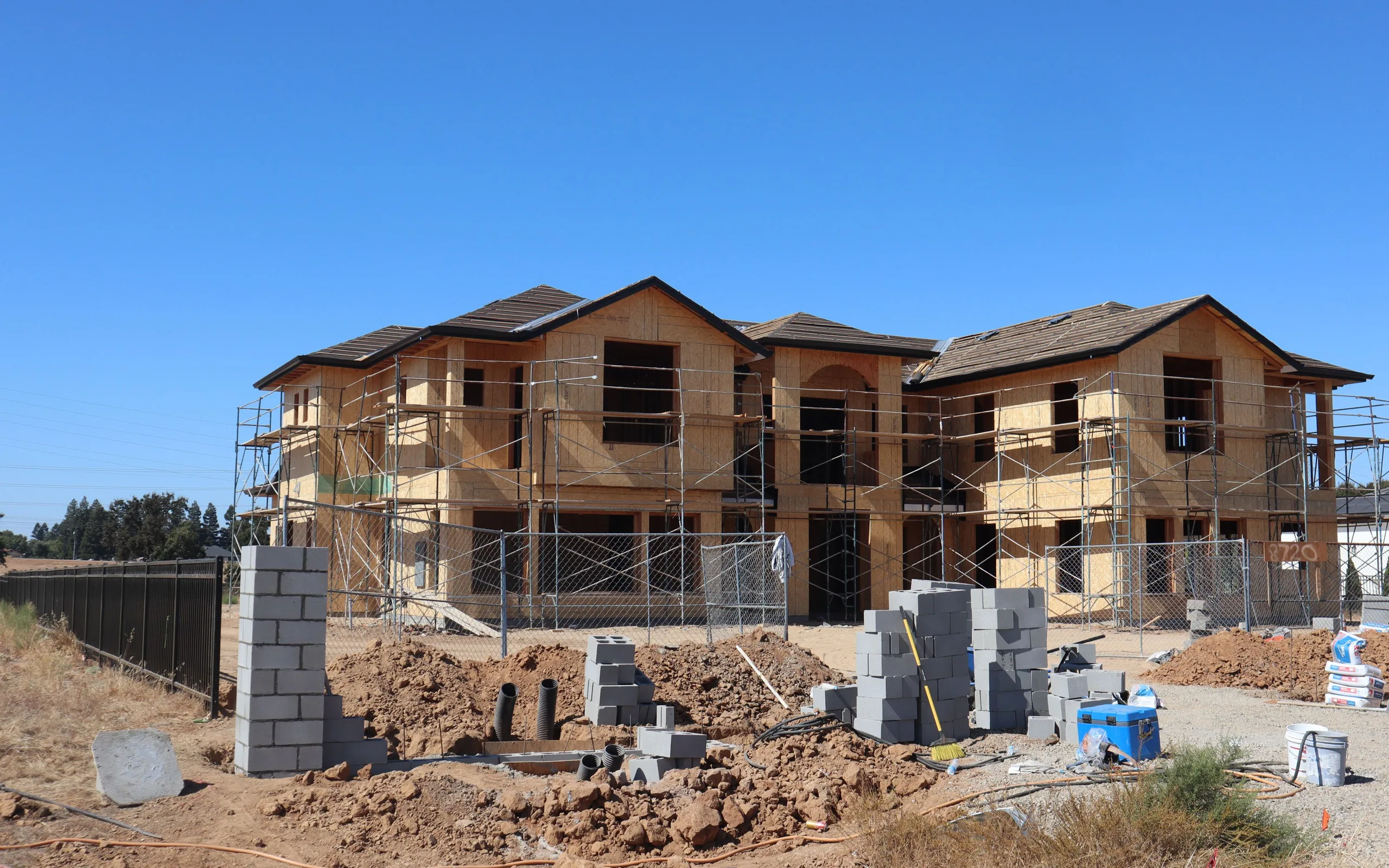 Façade d’une maison individuelle en travaux d’isolation par l’extérieur : échafaudage monté devant le mur et matériaux de chantier au sol.